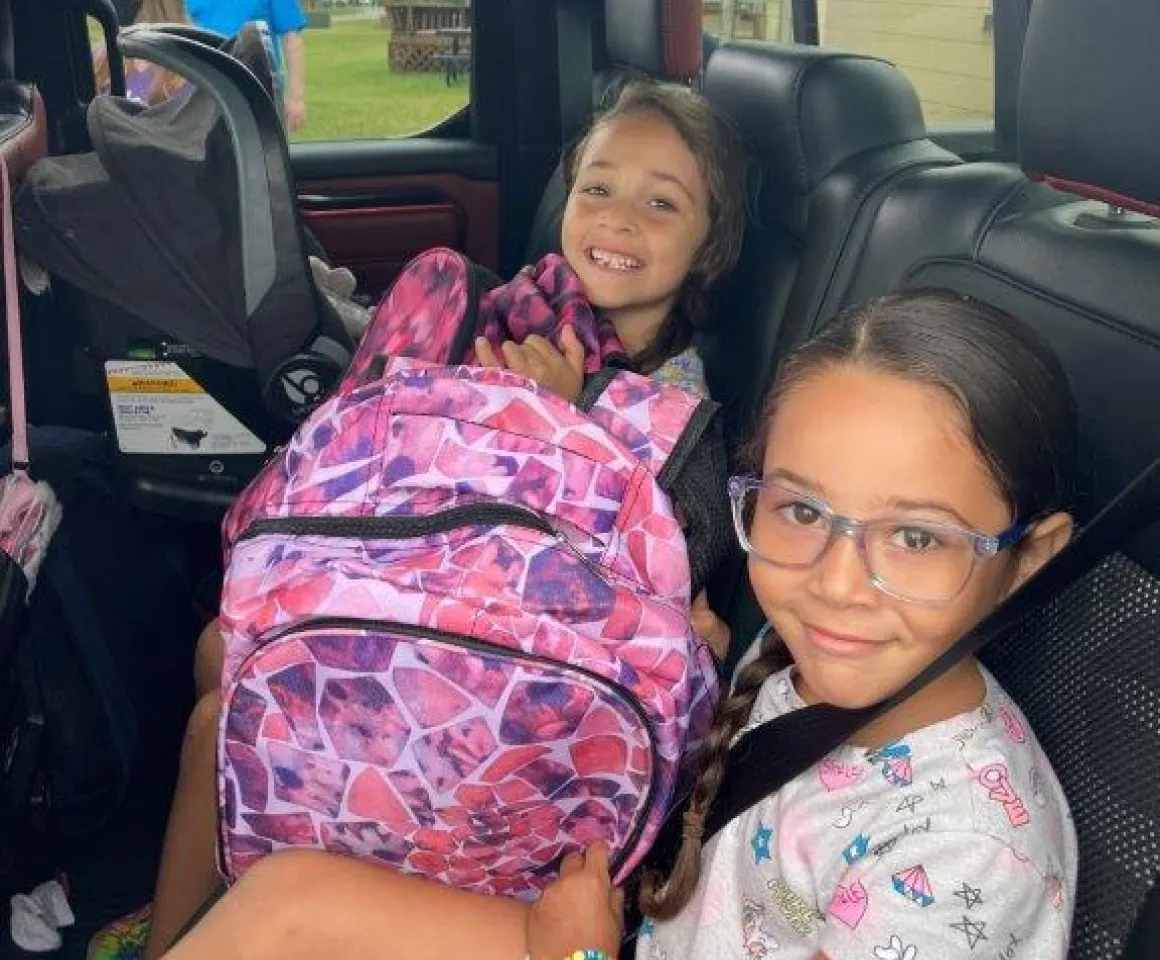Two young girls smiling in the back of a car